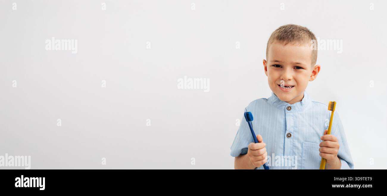 garçon souriant avec un espace dentaire naturel de bébé tenant deux brosses à dents colorées sur un fond blanc Banque D'Images