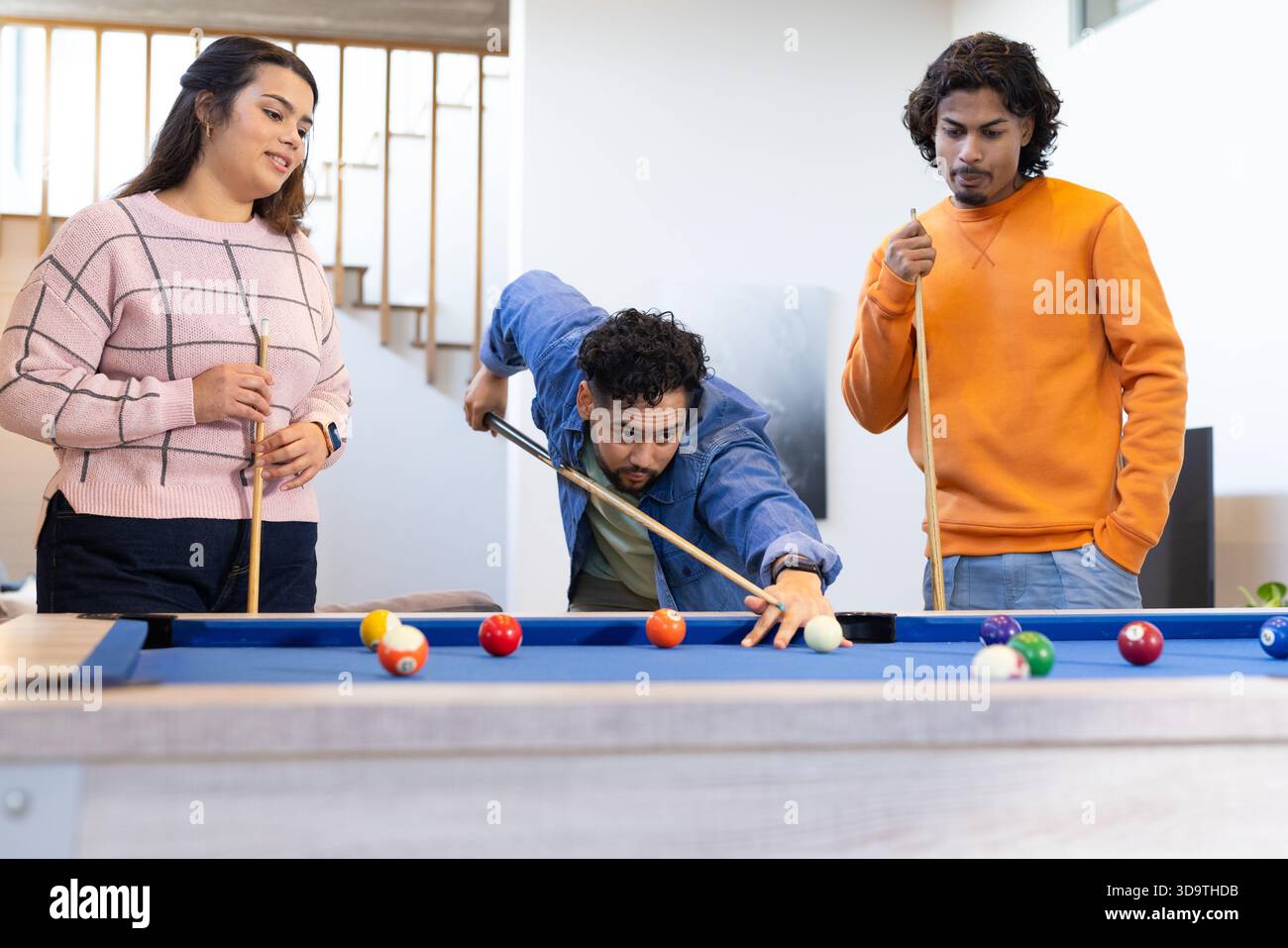 Amis jouant au billard avec des repères et des boules dispersées autour d'une table de billard en feutre bleu dans la salle de réception de la maison Banque D'Images