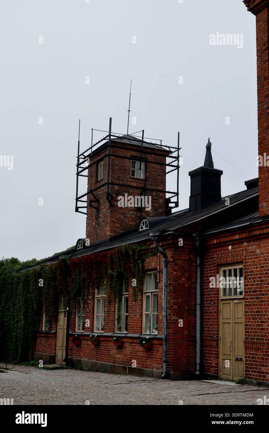 Bâtiment en briques rouges avec tour sur le toit et ossature en métal noir sous un ciel couvert par un matin brumeux à Suomenlinna Island, Helsinki, Finlande. Banque D'Images