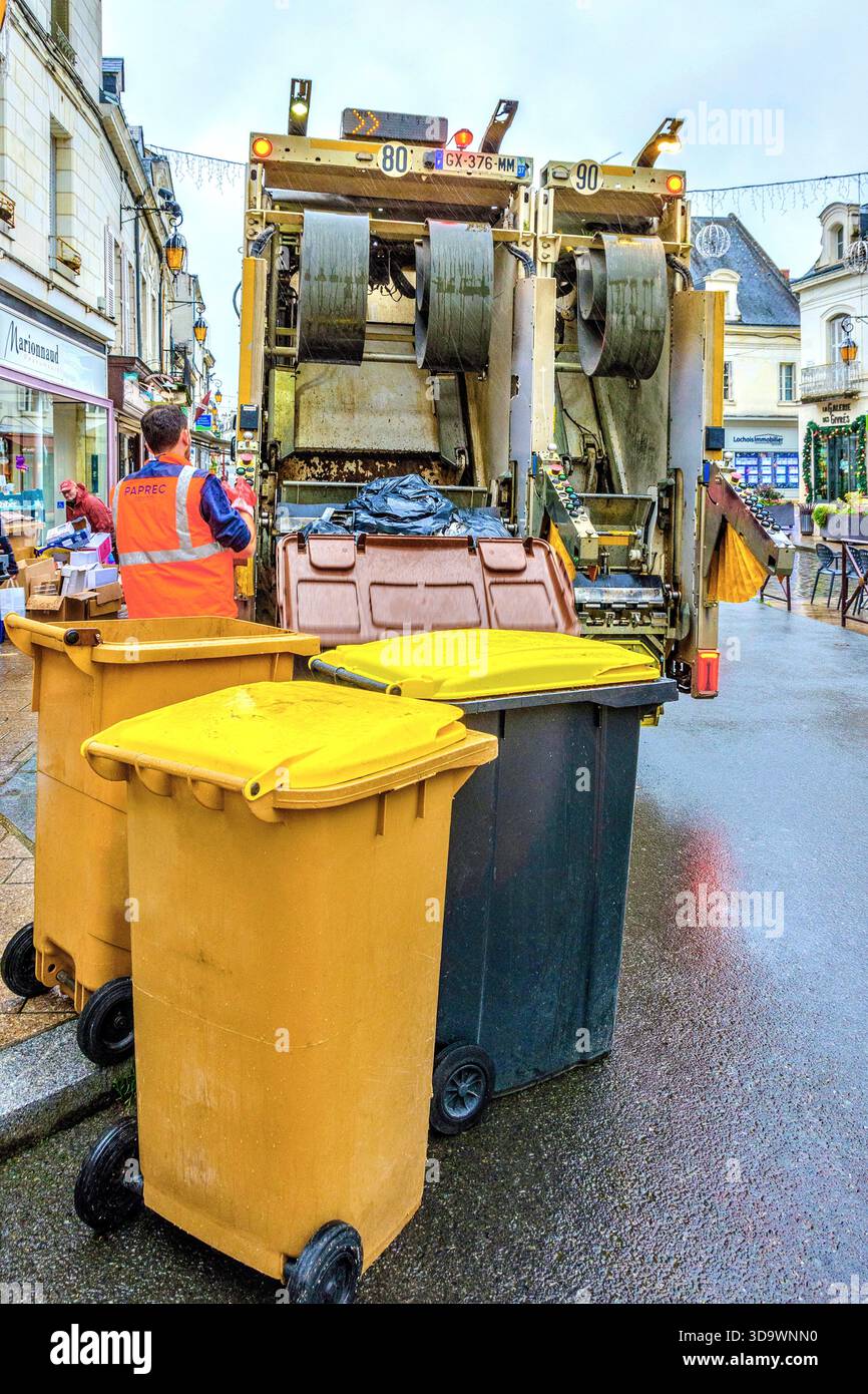 Travailleur municipal portant un gilet de sécurité orange chargeant un camion à ordures dans des poubelles à roulettes - Loches, Indre-et-Loire (37), France. Banque D'Images