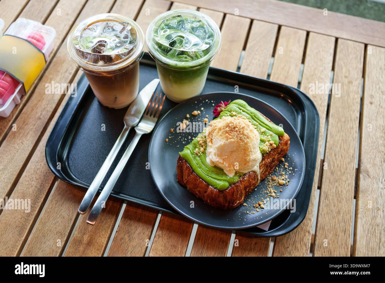 Ensemble de tranches de pain grillé garni de glace à la vanille, crème anglaise cuite à la vapeur avec café glacé, latte matcha glacé servi dans un plateau noir sur une table en bois Banque D'Images