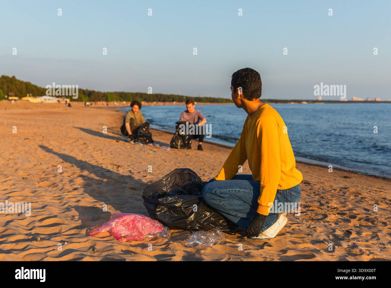 Jour de la Terre. L'équipe des activistes bénévoles collecte les ordures de la zone côtière de la plage. Femme Mans met des déchets en plastique dans un sac poubelle sur la rive de l'océan. Conservation de l'environnement nettoyage de la zone côtière || autorisation du modèle Banque D'Images