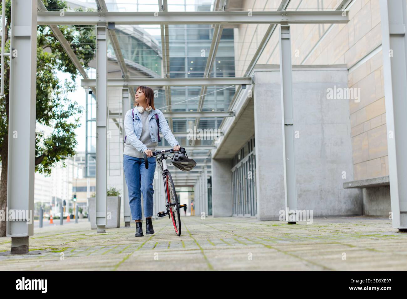 Femme asiatique marchant et poussant le vélo sur la passerelle sous la canopée à la façade du bureau Banque D'Images