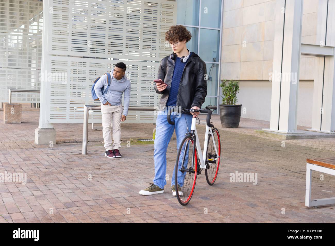 Divers amis s'appuyant contre la rampe dans la cour, ami vérifiant smartphone à côté du vélo, espace de copie Banque D'Images
