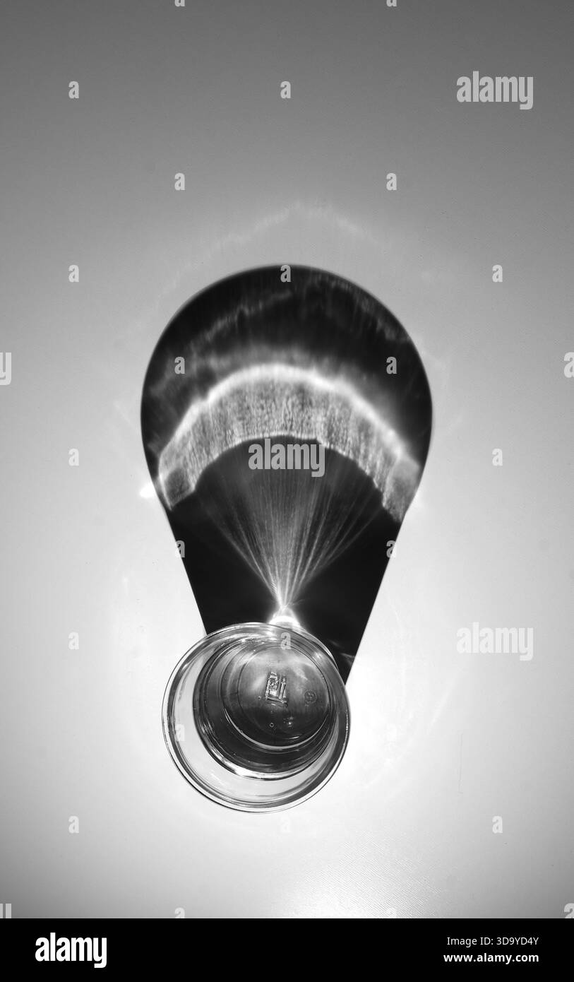 Verre avec un tiers d'huile, d'eau et de vide projetant une ombre à partir d'une seule source de lumière. Banque D'Images