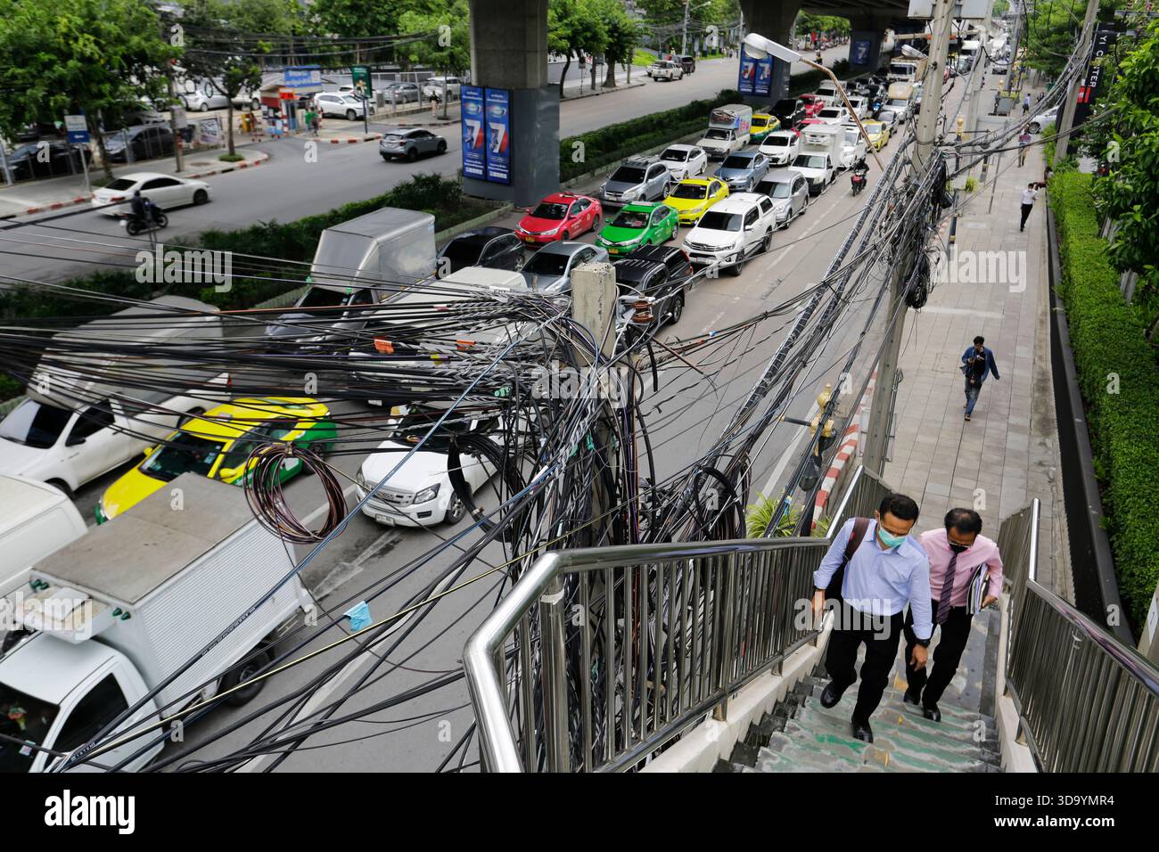 Bangkok, Thaïlande - 15 juillet 2022 : les gens marchent à côté de câbles de transmission d'énergie électrique et de communication attachés à un poteau de rue. Banque D'Images