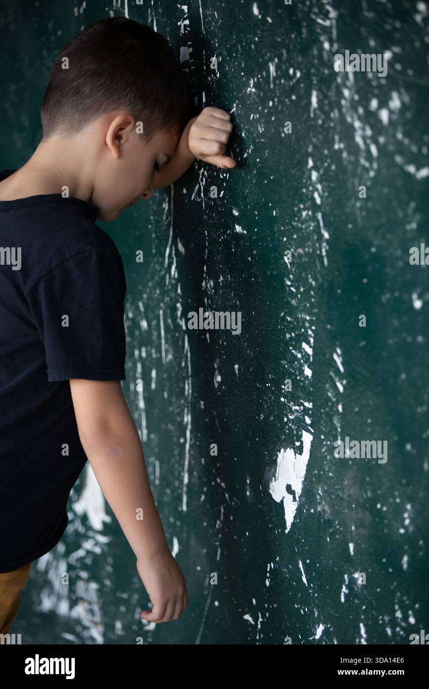 Garçon triste appuyé contre la tête de mur délabrée dans les mains Banque D'Images