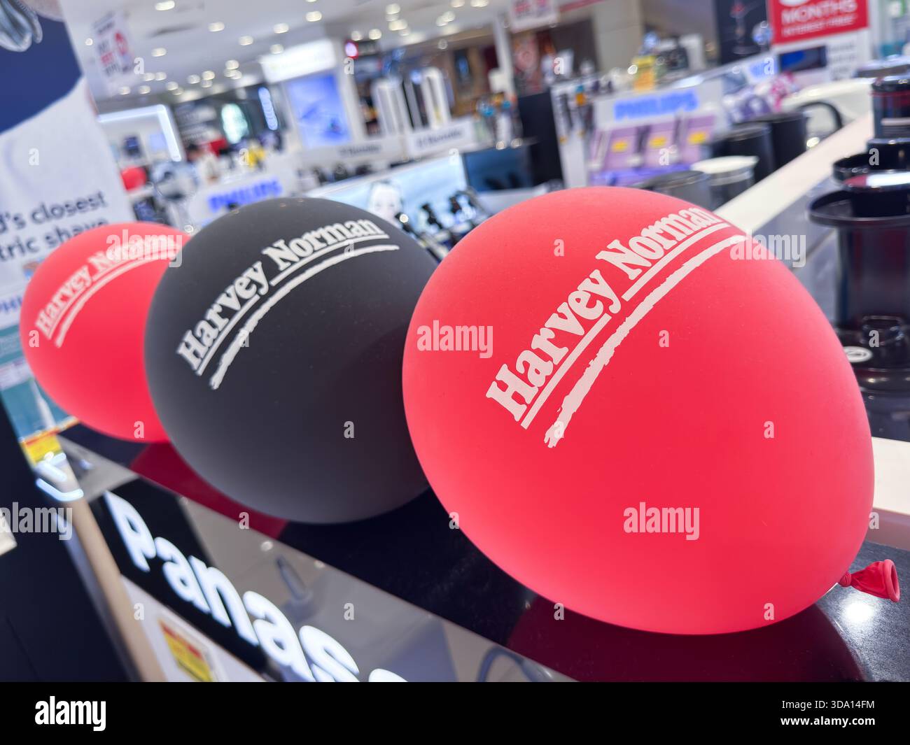 Penang, Malaisie - 7 juillet 2025 : trois ballons en rouge, noir et blanc sont disposés sur un comptoir à HARVEY NORMAN, améliorant ainsi l'environnement commercial Banque D'Images