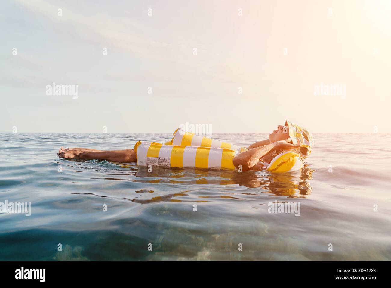 Femme, flotteur gonflable, Océan - détente sur un flotteur gonflable rayé jaune et blanc dans l'océan. Banque D'Images