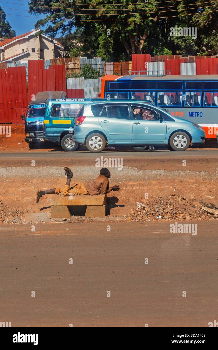 Homme couché sur un banc par une route de ville avec circulation Banque D'Images
