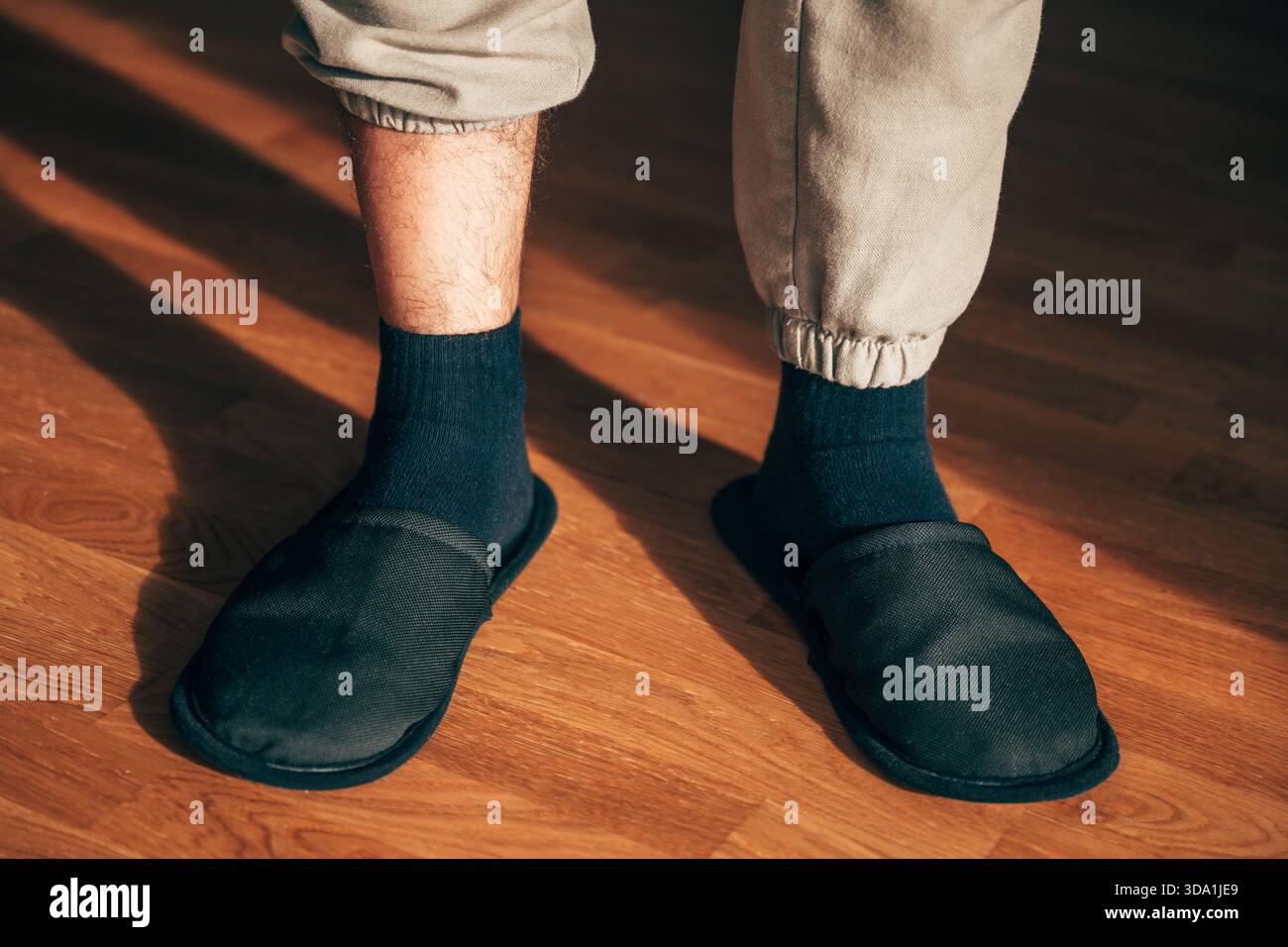 Vue à angle bas d'un homme détendu portant des chaussettes noires confortables sur des chaussettes sombres, debout sur des planches en bois chaudes avec des ombres spectaculaires de la lumière du soleil. Sele Banque D'Images