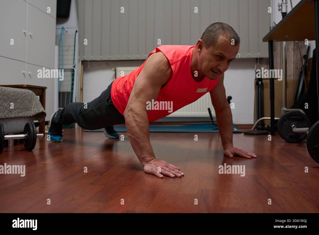 Homme athlétique d'âge moyen effectuant un exercice de push-up sur le sol de la salle de séjour avec un équipement de gymnastique à domicile Banque D'Images