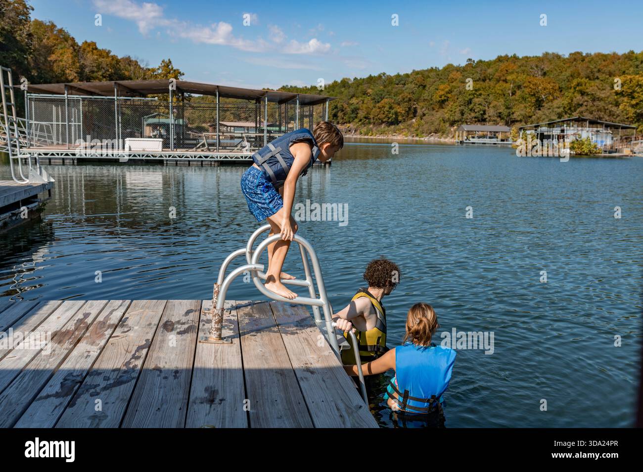 Enfant et adolescents en gilets de sauvetage se préparant à nager depuis le quai au bord du lac Banque D'Images