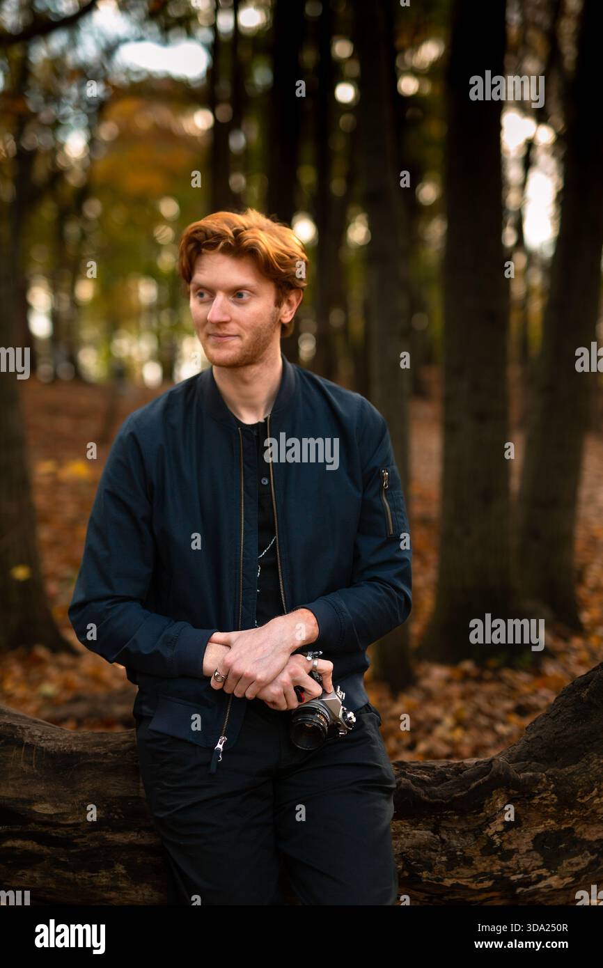 Le jeune homme aime se promener en automne dans une forêt tout en tenant un appareil photo Banque D'Images