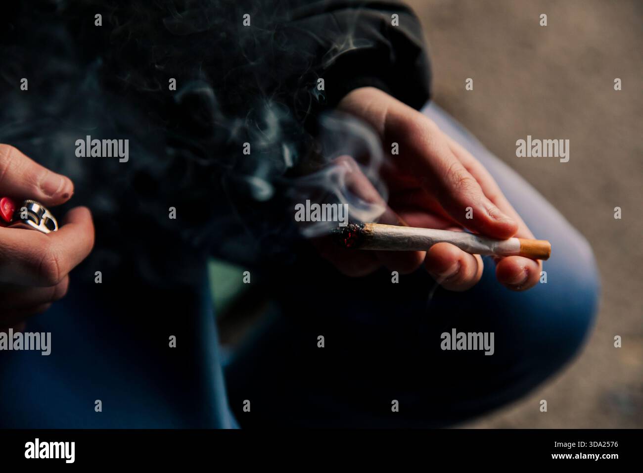 mains tenant une cigarette de marijuana fraîchement allumée et soufflant de la fumée Banque D'Images