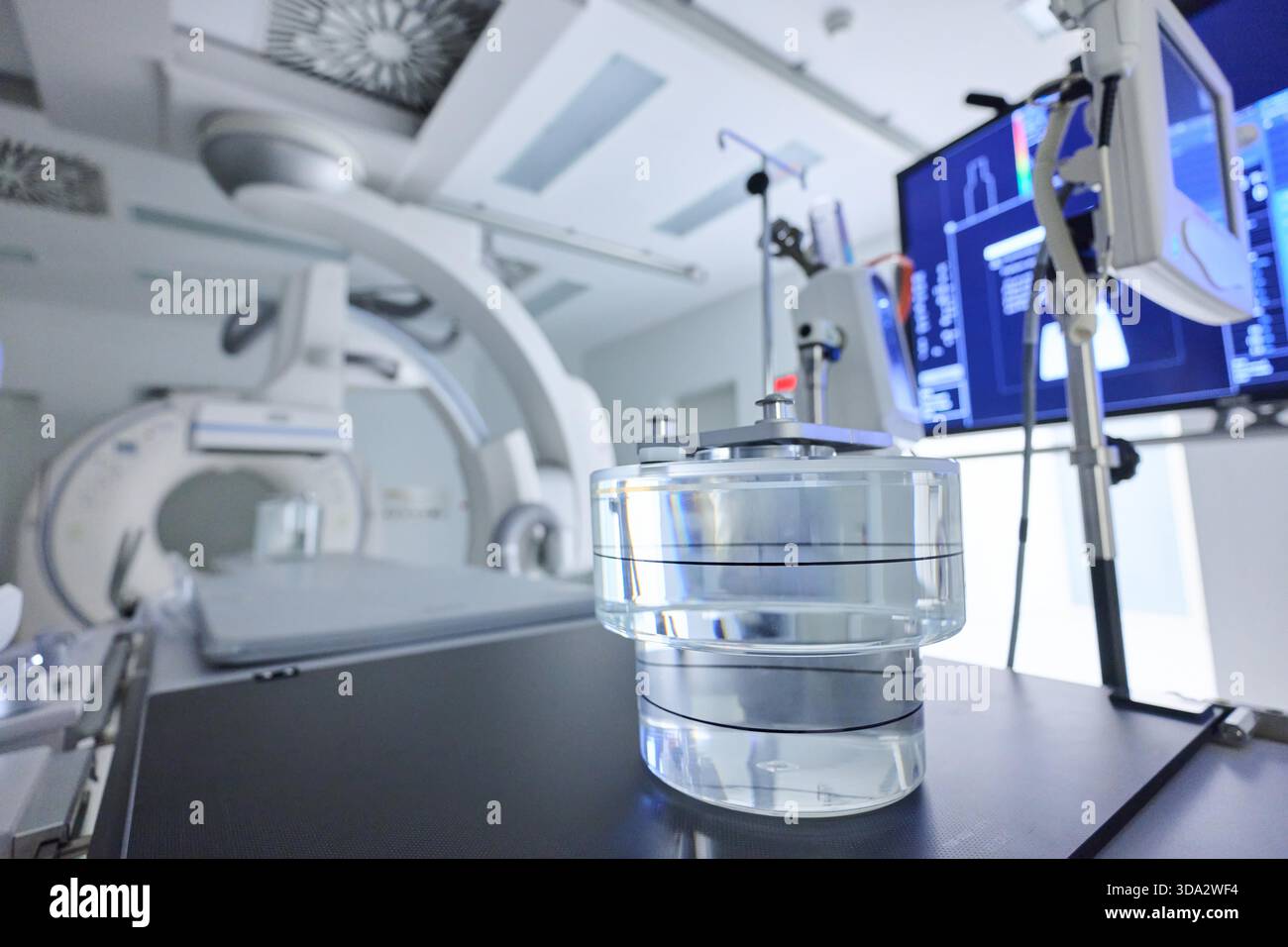 Une salle clinique propre et moderne dispose d'un équipement d'imagerie avancé. Un récipient transparent repose bien en évidence sur la table, utilisé pour les techniques d'imagerie médicale. Banque D'Images