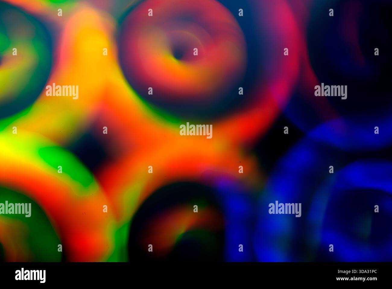 Image abstraite de formes de lumière circulaire tourbillonnantes floues dans les tons rouge, vert, bleu et jaune, se chevauchant sur un fond sombre avec des dégradés lisses, Banque D'Images