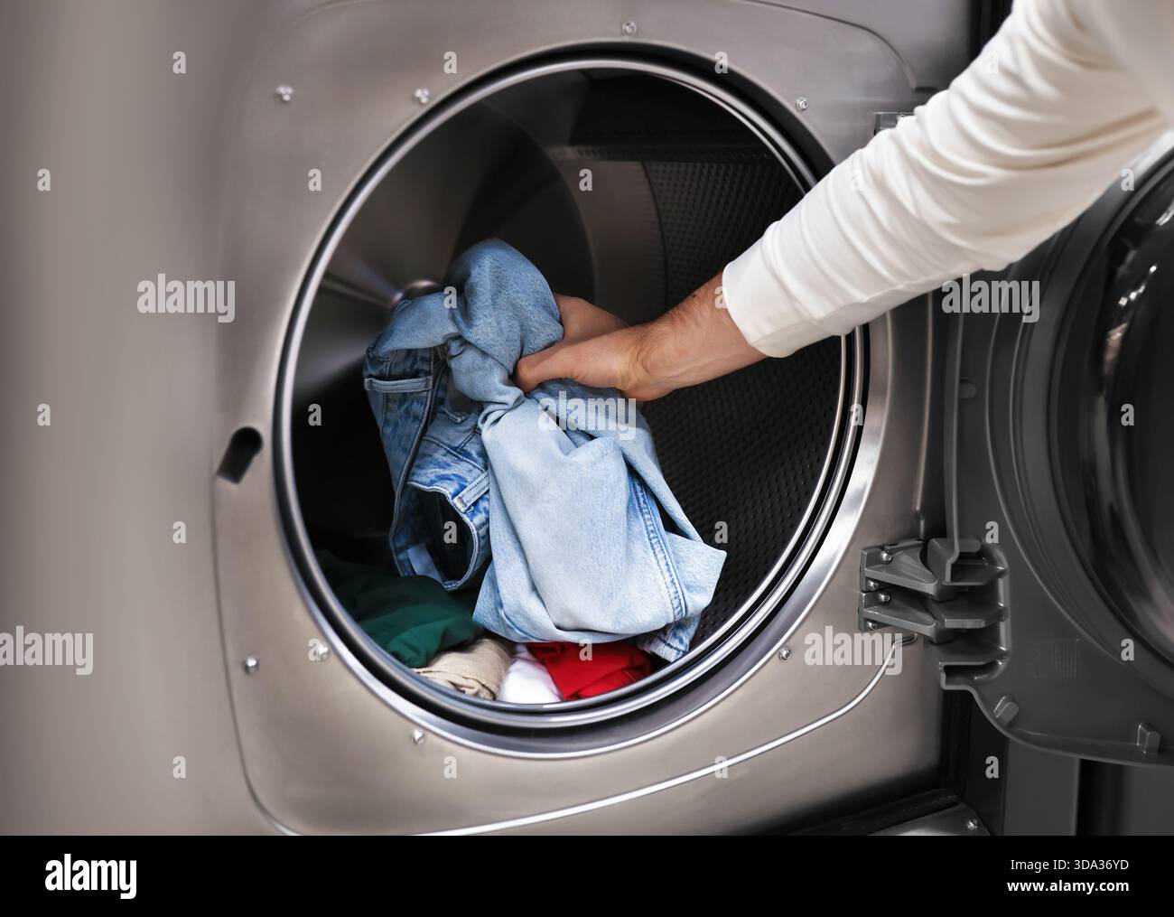 Gros plan de la main d'un homme chargeant des jeans et des vêtements bleus dans une machine à laver moderne. Photo de haute qualité Banque D'Images