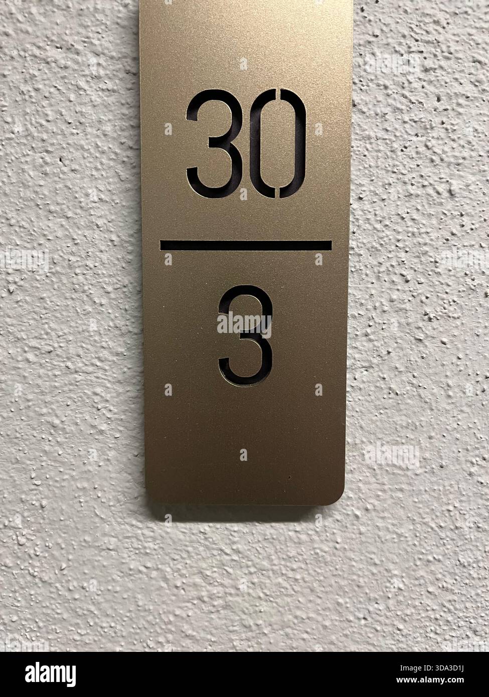 Panneau d’appartement en métal doré sur un mur texturé blanc montrant la plaque d’immatriculation “30 / 3” mots-clés : - Image de stock capturée avec un smartphone