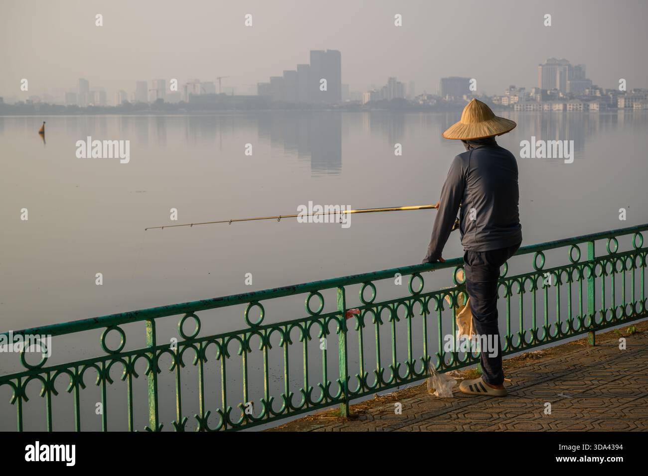 Un pêcheur vietnamien solitaire portant un chapeau conique au lac brumeux de l'Ouest, Hanoi, Vietnam Banque D'Images