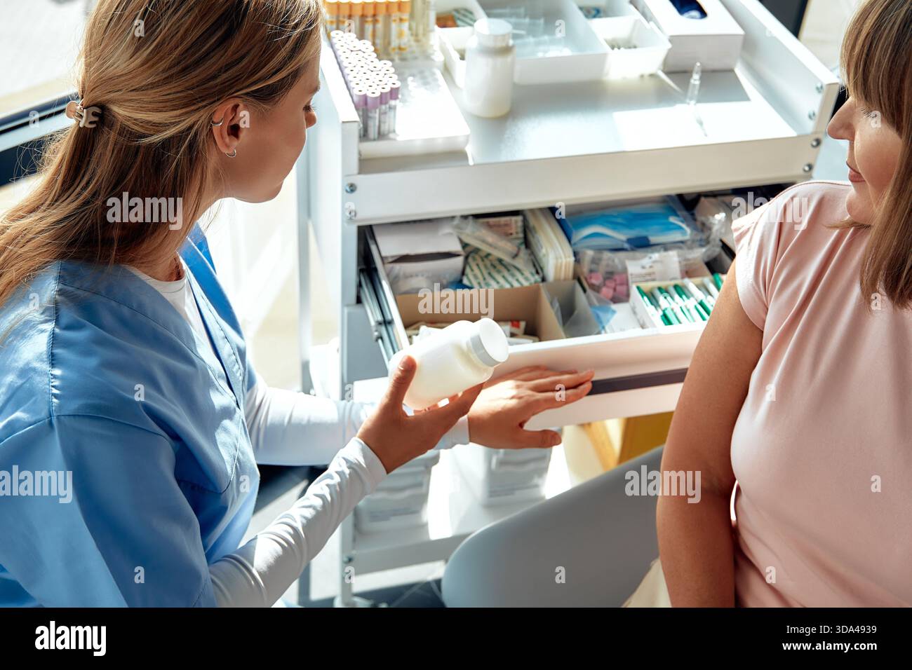 Un professionnel de la santé dans les gommages et les gants remet une bouteille d'ordonnance à un patient, soulignant l'importance de la gestion appropriée des médicaments fo Banque D'Images