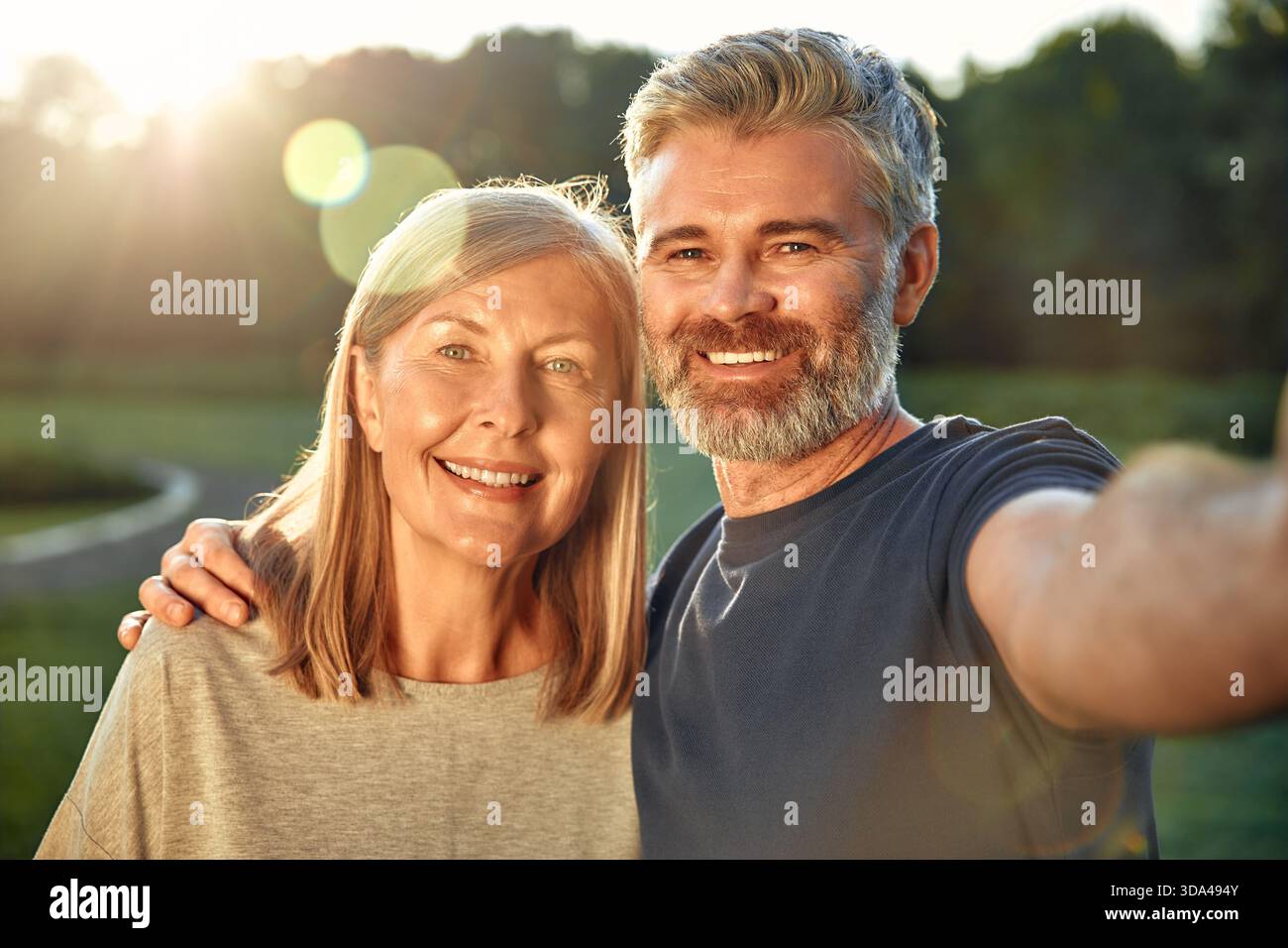 Par une journée ensoleillée dans un parc animé, une femme âgée joyeuse et un homme d'âge intermédiaire prennent un selfie, chérissant leurs moments au milieu de la nature magnifique, cap Banque D'Images