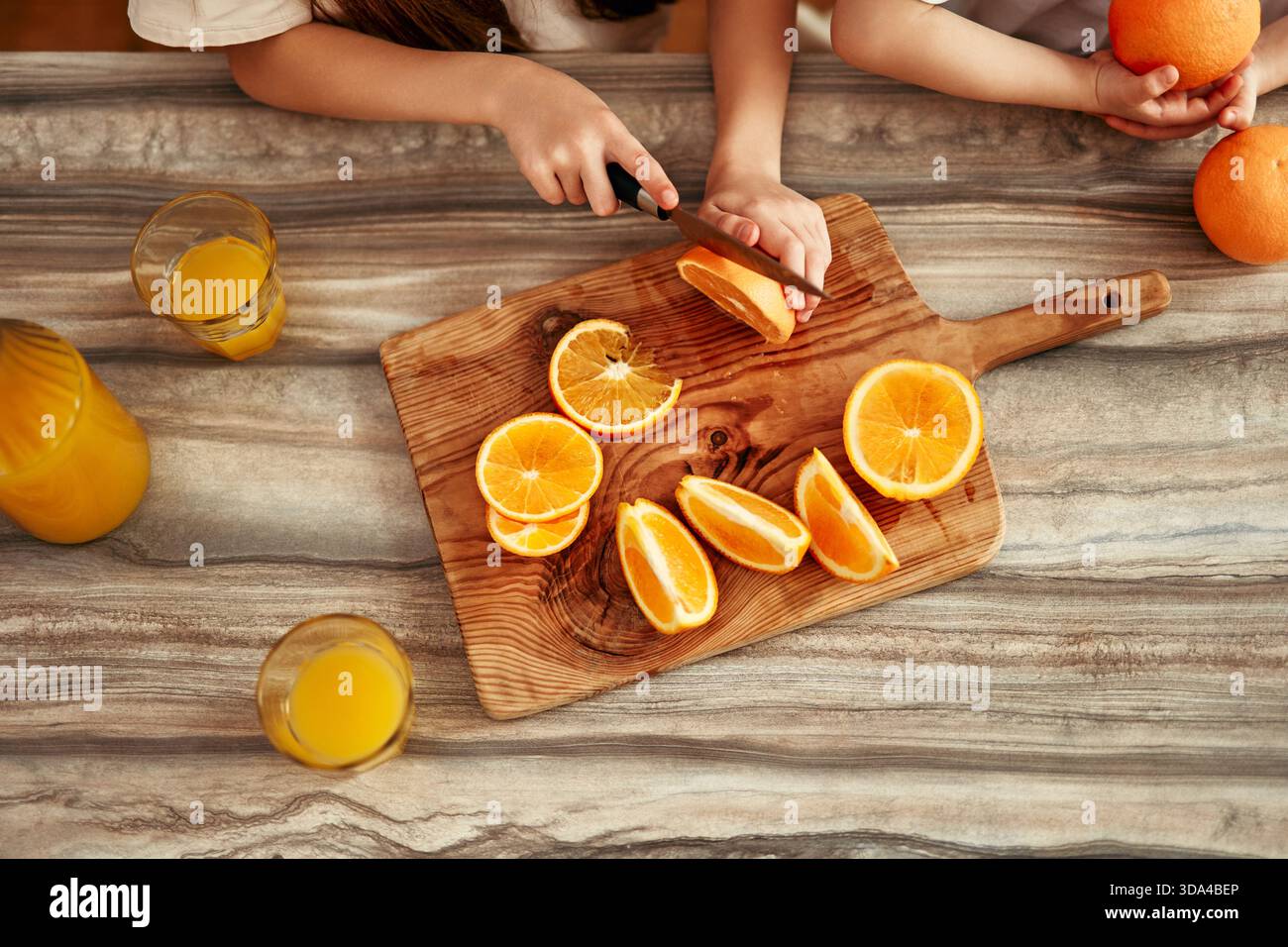 Deux enfants sont dans la cuisine lumineuse coupant des oranges pour faire du jus, symbolisant un style de vie familial heureux et sain centré sur la bonne maison Banque D'Images