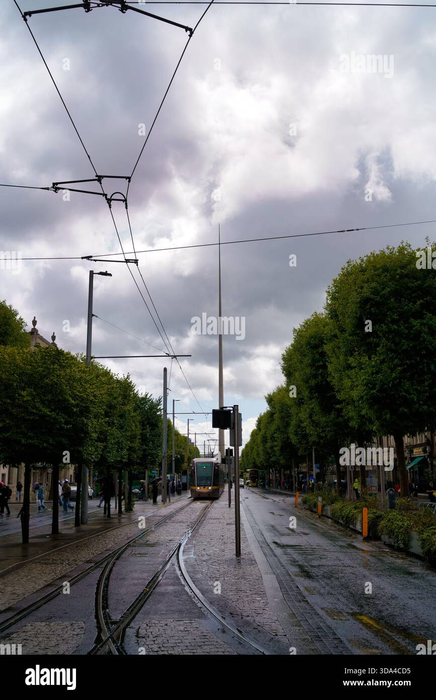 Un tramway descend une rue baignée de pluie à Dublin, encadrée par des arbres et des lignes électriques aériennes. Dublin, Irlande, 2025-08-08 Banque D'Images