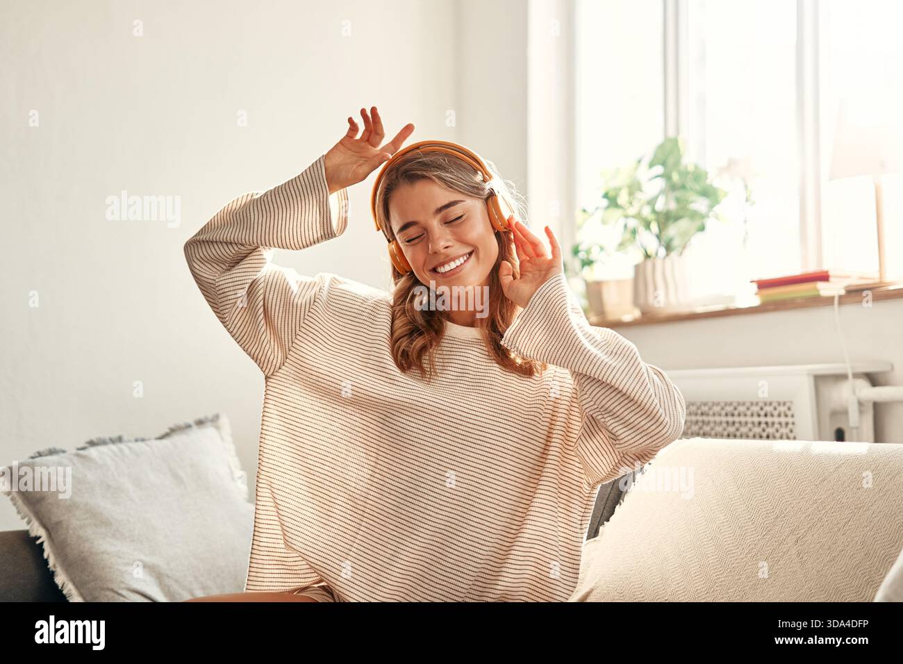 Jeune femme écoutant de la musique ou une leçon audio dans un casque tout en étant assise sur le sol près du canapé dans le salon à la maison. Banque D'Images