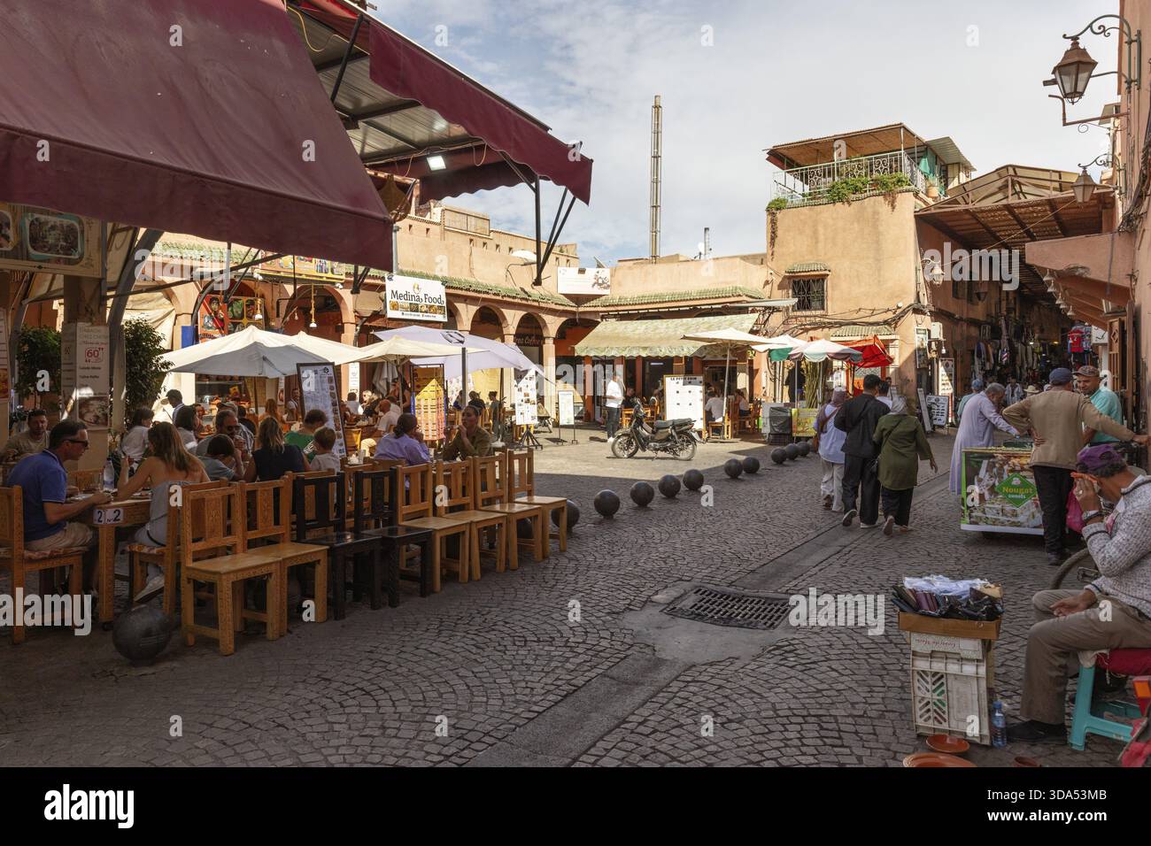 Ambiance conviviale dans une rue avec des restaurants en plein air et des gens autour de tables Banque D'Images