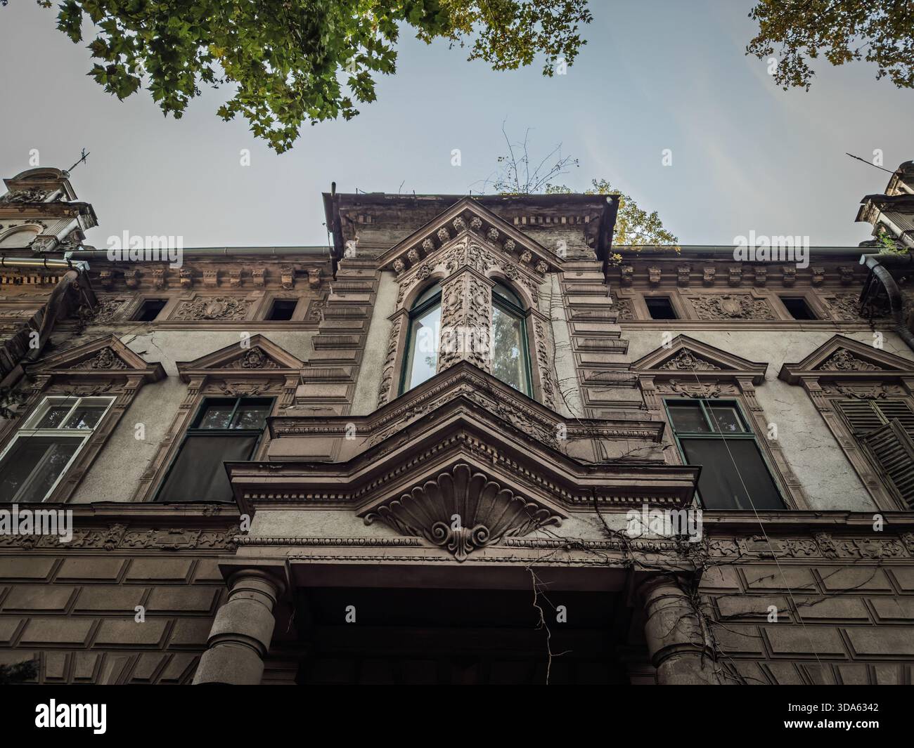 Vue rapprochée d'une façade résidentielle en décomposition dans le centre-ville de Subotica, Serbie, montrant de la peinture écaillée, du plâtre fissuré, de la corniche ornée et des fenêtres vieillissantes, Banque D'Images