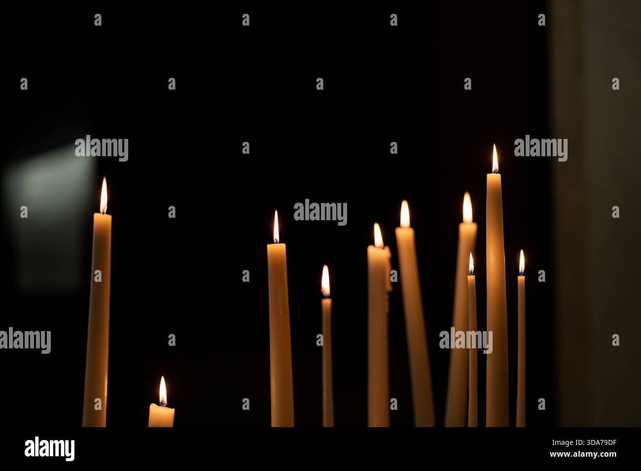 Bougies allumées dans l'obscurité à l'intérieur d'une église tranquille. Flammes chaudes aux chandelles illuminant un espace sacré sombre. Banque D'Images