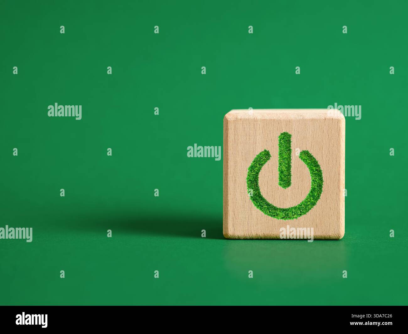 Cube en bois sur fond vert affichant le symbole de puissance fabriqué à partir d'herbe verte, représentant l'énergie durable et l'écologie. Démarrage de l'environnement pro Banque D'Images
