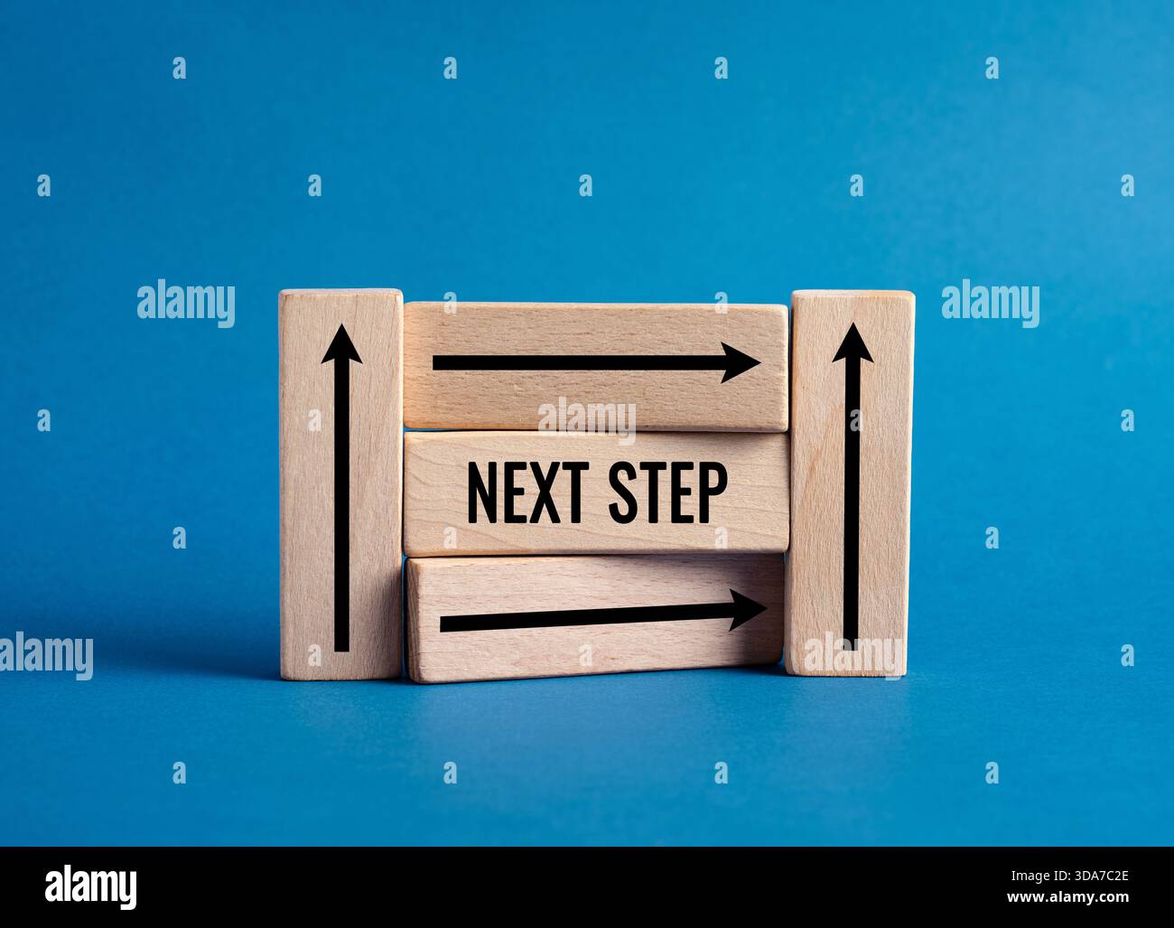 Blocs en bois affichant le texte de L'ÉTAPE SUIVANTE avec des flèches, symbolisant le choix de la direction, de la progression, de la stratégie et du développement en avant sur un fond bleu Banque D'Images