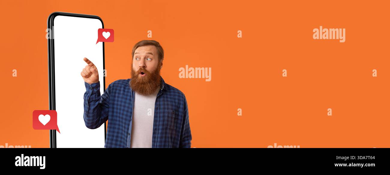 Homme excité pointant vers smartphone affichant les réactions des médias sociaux sur fond orange éclatant Banque D'Images