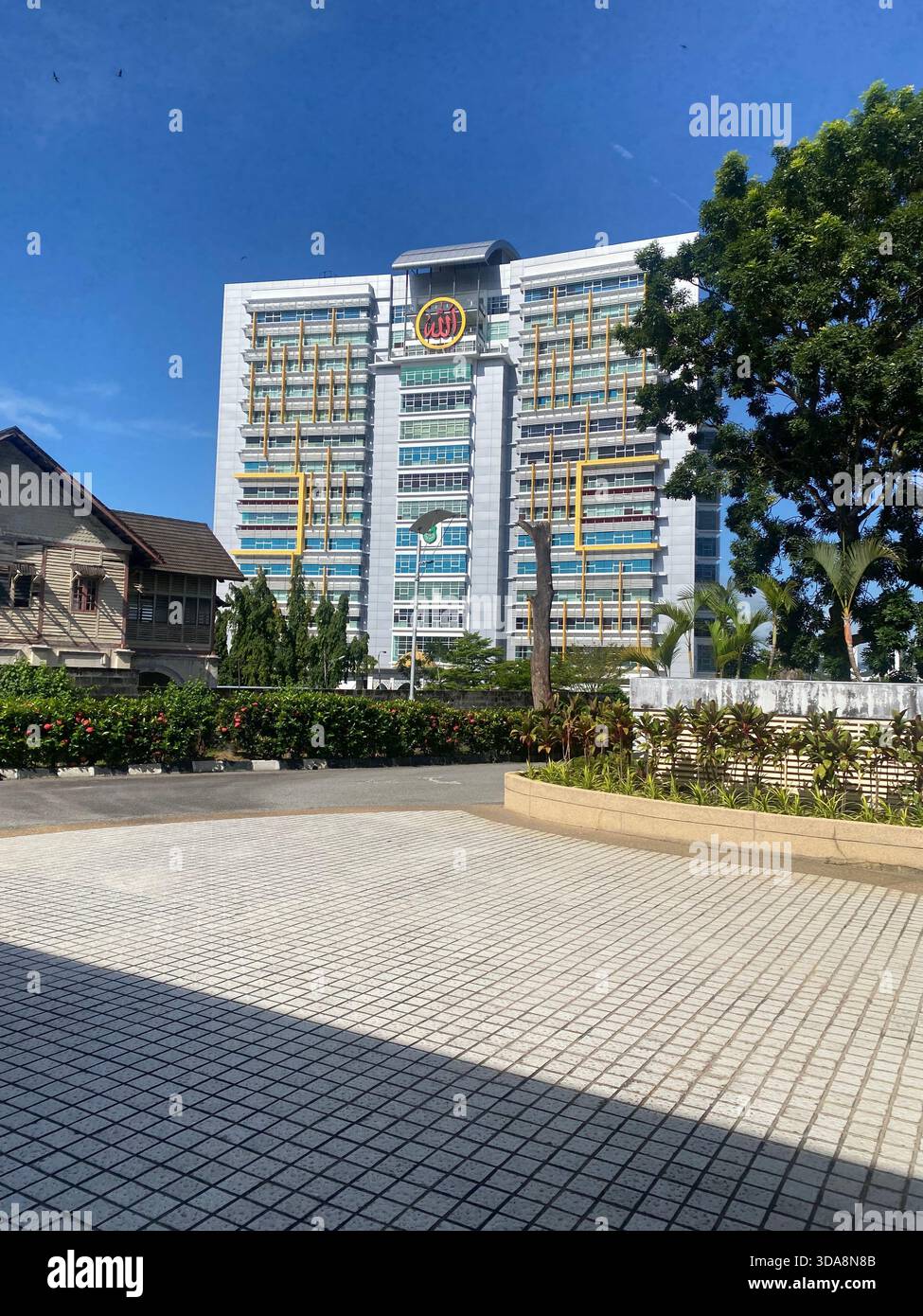 Bâtiment gouvernemental moderne de grande hauteur avec emblème de calligraphie islamique, entouré de verdure sous un ciel bleu clair. - Image de stock capturée avec un smartphone