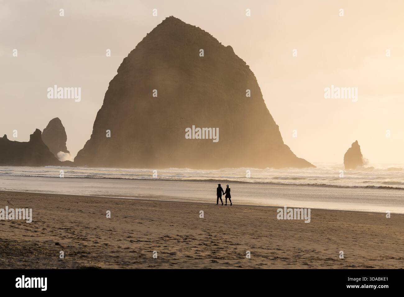 Couple marchant le long de la plage à Cannon Beach avec Haystack Rock s'élevant à travers la brume côtière, Oregon, États-Unis. Banque D'Images