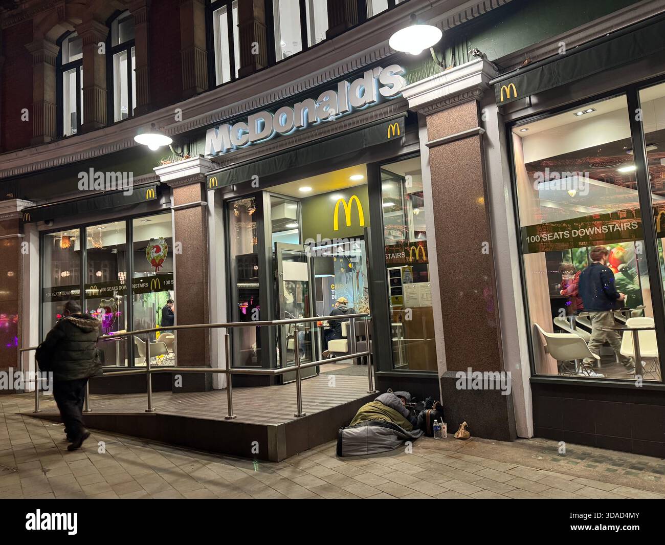 Un restaurant McDonald's sur Charing Cross à Londres, tandis qu'un sans-abri dort dans une porte à l'extérieur dans une rue de la ville. Banque D'Images