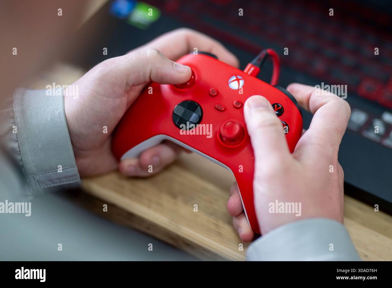 Gros plan d'un enfant tenant une manette Xbox rouge et noire connectée par un câble USB rouge. Banque D'Images