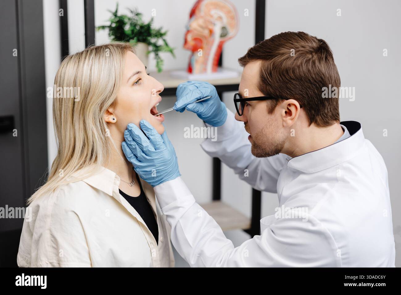 Médecin utilisant une spatule d'inspection pour examiner la gorge du patient. ORL médecin faisant l'examen de gorge d'une femme. La patiente a ouvert la bouche jusqu'à la gorge. Banque D'Images