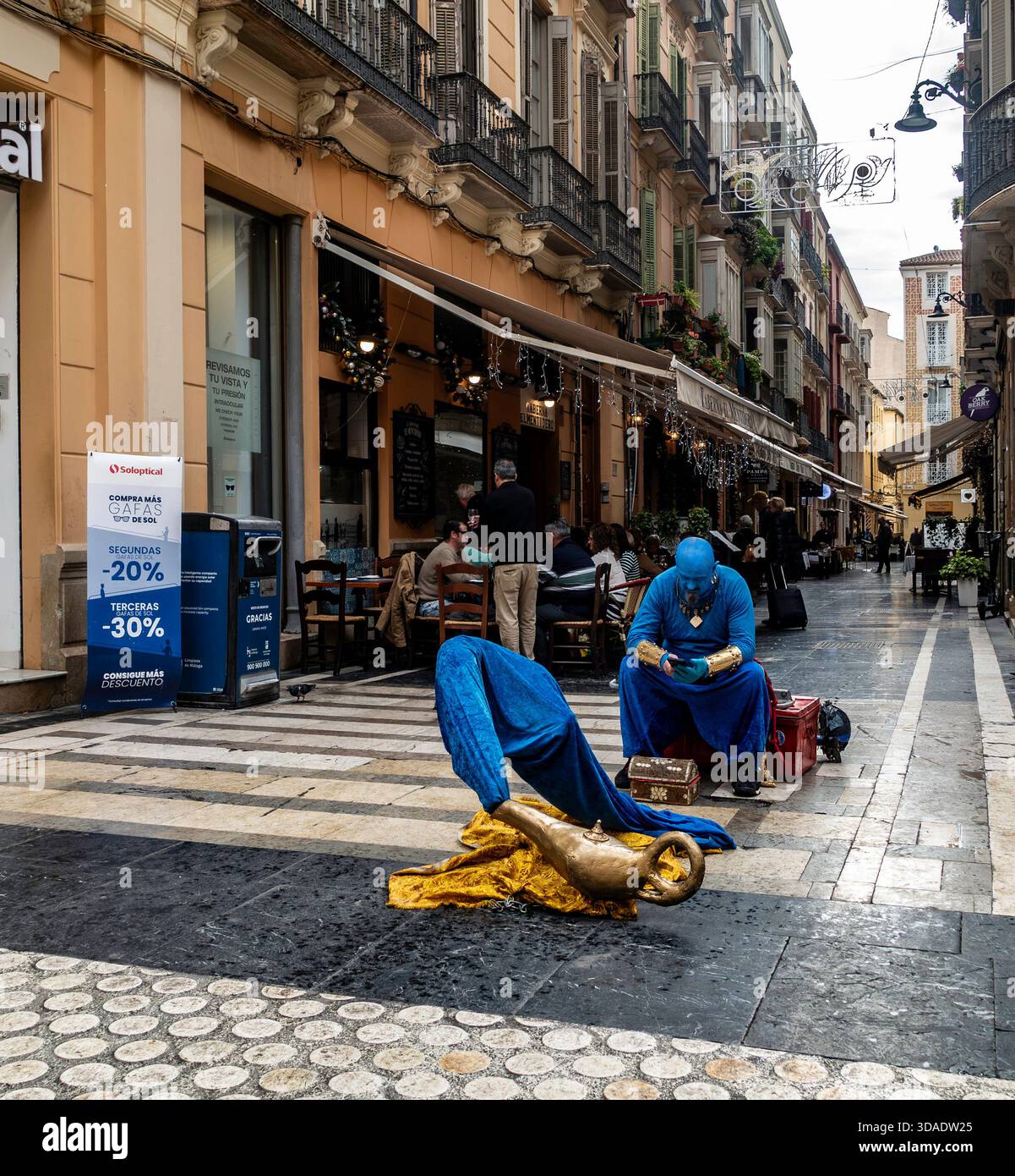 Blue Genie Street performer est assis près de la lampe en laiton. Malaga, Espagne, rue pavée. Chaussée humide, centre historique, Banque D'Images