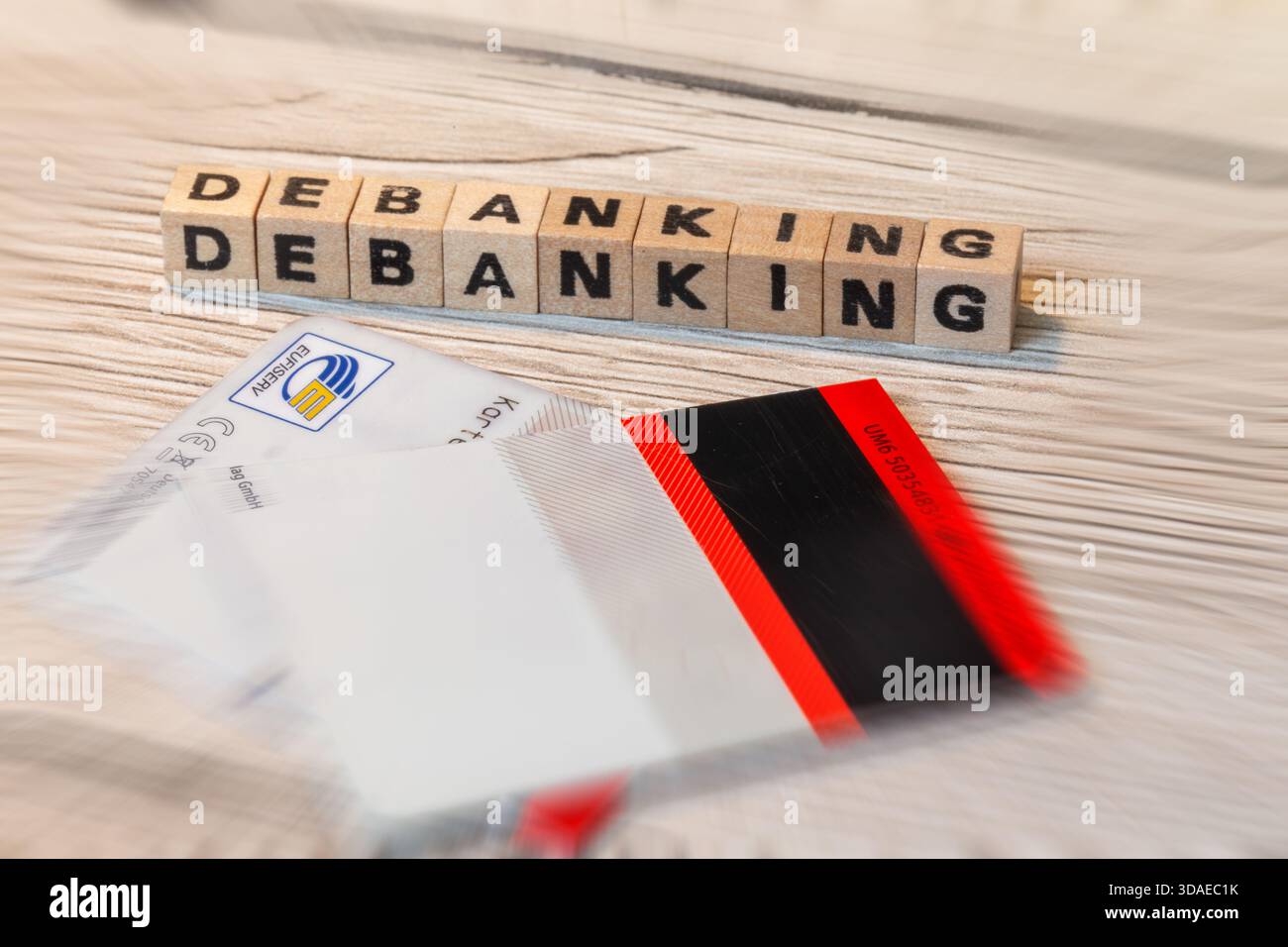 Image de symbole de debanking : des cubes de lettres devant une carte de paiement découpée épellent le mot DEBANKING Banque D'Images