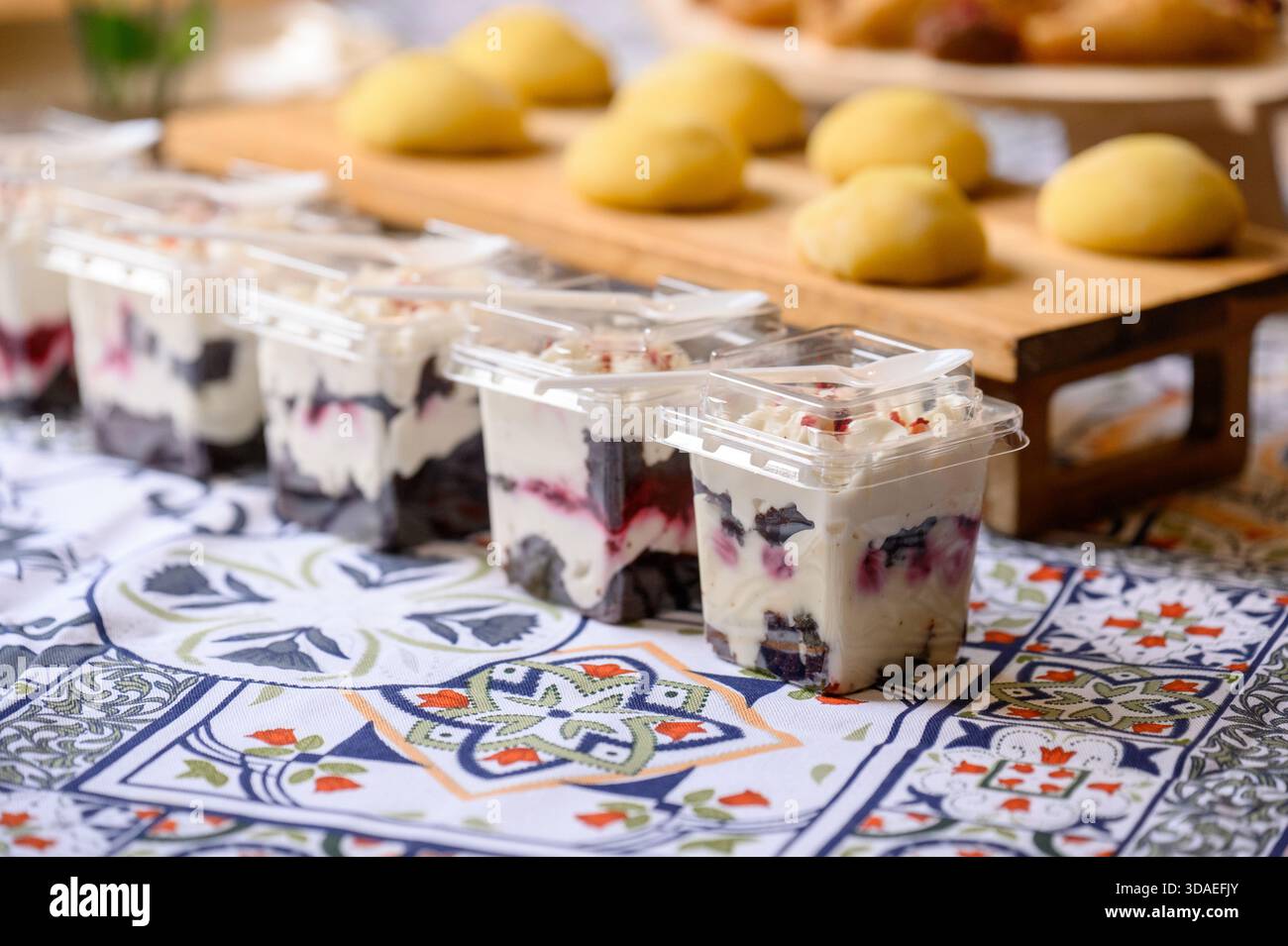 Desserts en portions avec des baies et de la crème dans des tasses en plastique sur une nappe à motifs à une table de buffet. Gros plan de baies et de créa emballés individuellement Banque D'Images