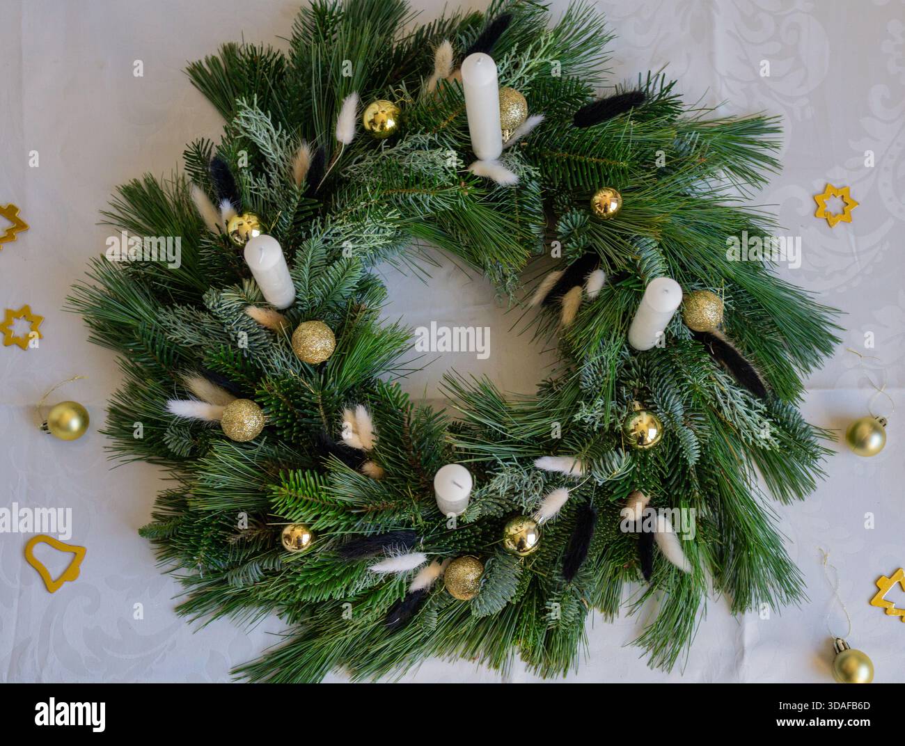Vue de dessus d'une couronne de l'Avent à feuilles persistantes décorée de bougies blanches, de boules dorées et de feuillage naturel. Les branches d'épinette et de pin créent une fête. Banque D'Images