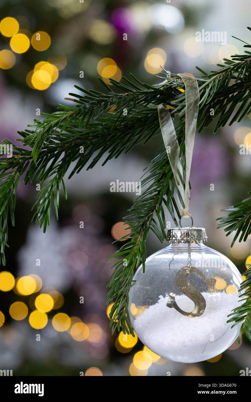 Gold S pour boule de Noël Santa accrochée à une branche de pin avec des lumières bokeh dorées chaudes en arrière-plan, élégante décoration de vacances festive Banque D'Images