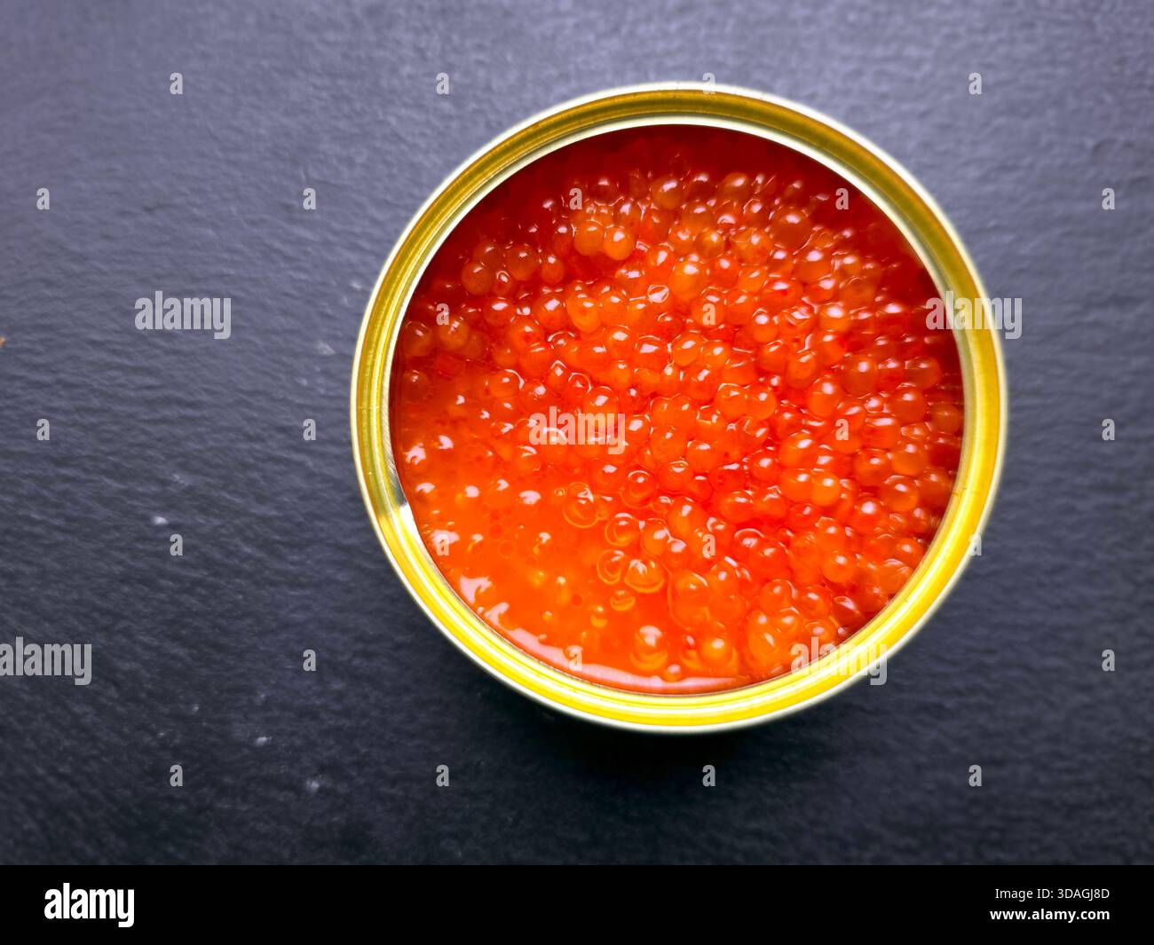 Un pot rempli de caviar de saumon rouge repose sur une surface sombre, prêt à être partagé pendant un repas ou une cueillette. Ce caviar est parfait pour les apéritifs et sn Banque D'Images