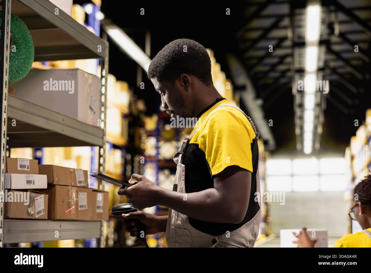 Employé afro-américain scannant des colis dans un grand entrepôt, enregistrant les détails de l'expédition des factures de transport aérien dans les registres des dépôts industriels. Utilisation du scanner pour l'exécution des commandes. Banque D'Images