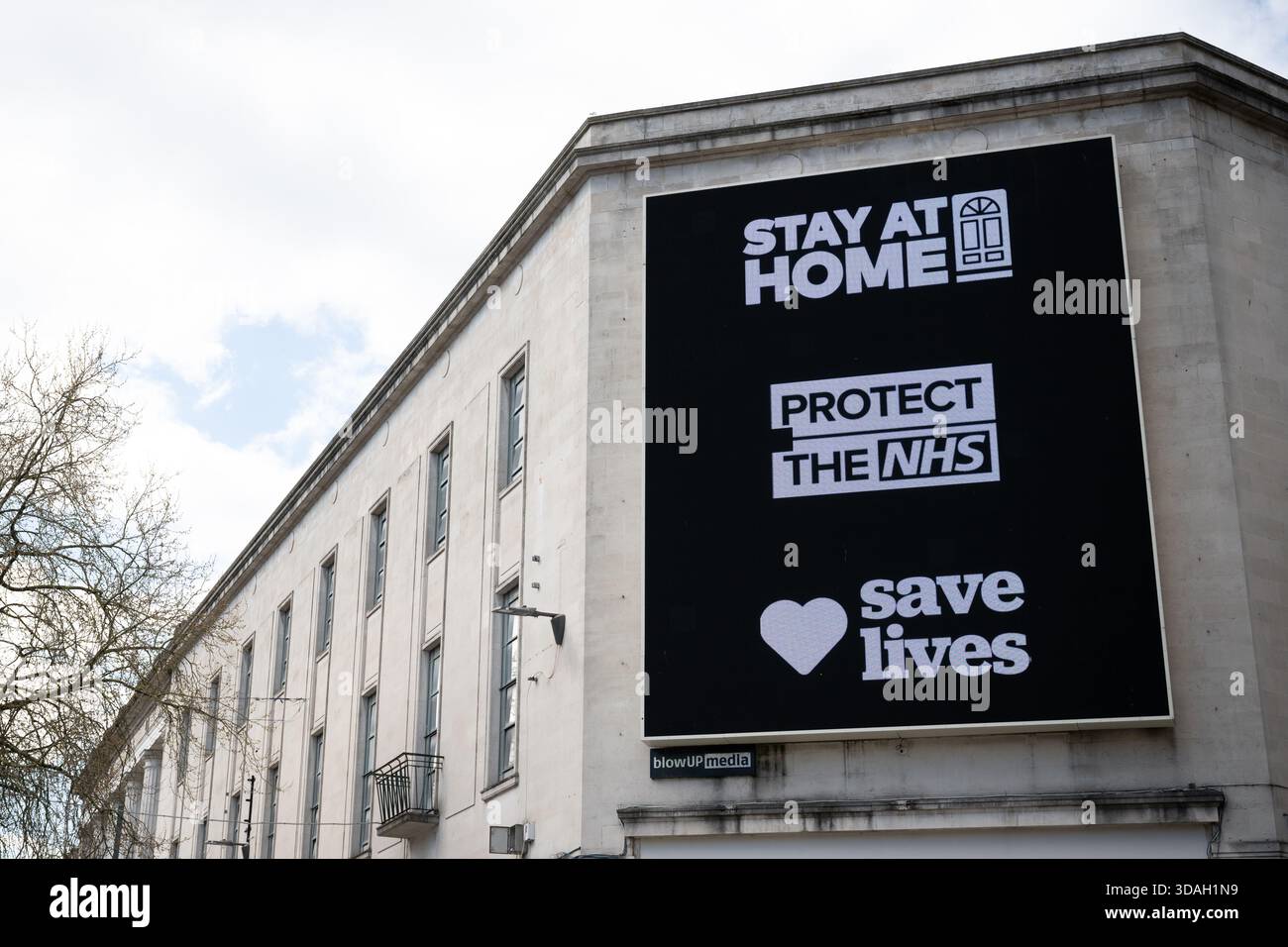 Un grand panneau d'affichage noir affiche bien en évidence le message « RESTEZ À LA MAISON » au-dessus de « PROTÉGEZ LE NHS » et « SAUVEZ DES VIES » avec un symbole de cœur entre les deux sur le Qué Banque D'Images