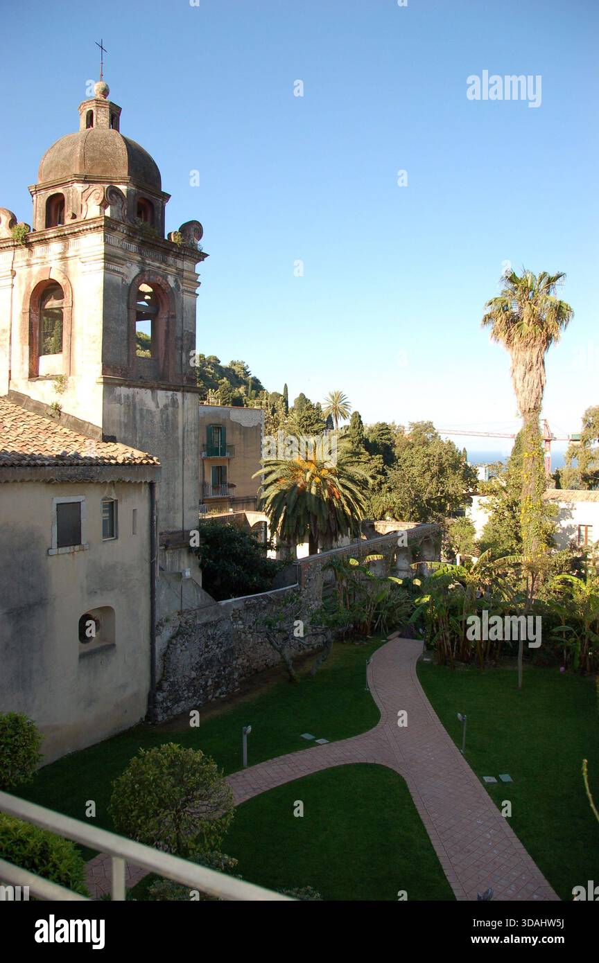 Clocher de l'église historique à Taormina, Sicile, entouré de palmiers et de vieux bâtiments en pierre, mettant en valeur l'architecture méditerranéenne sous un ciel Banque D'Images
