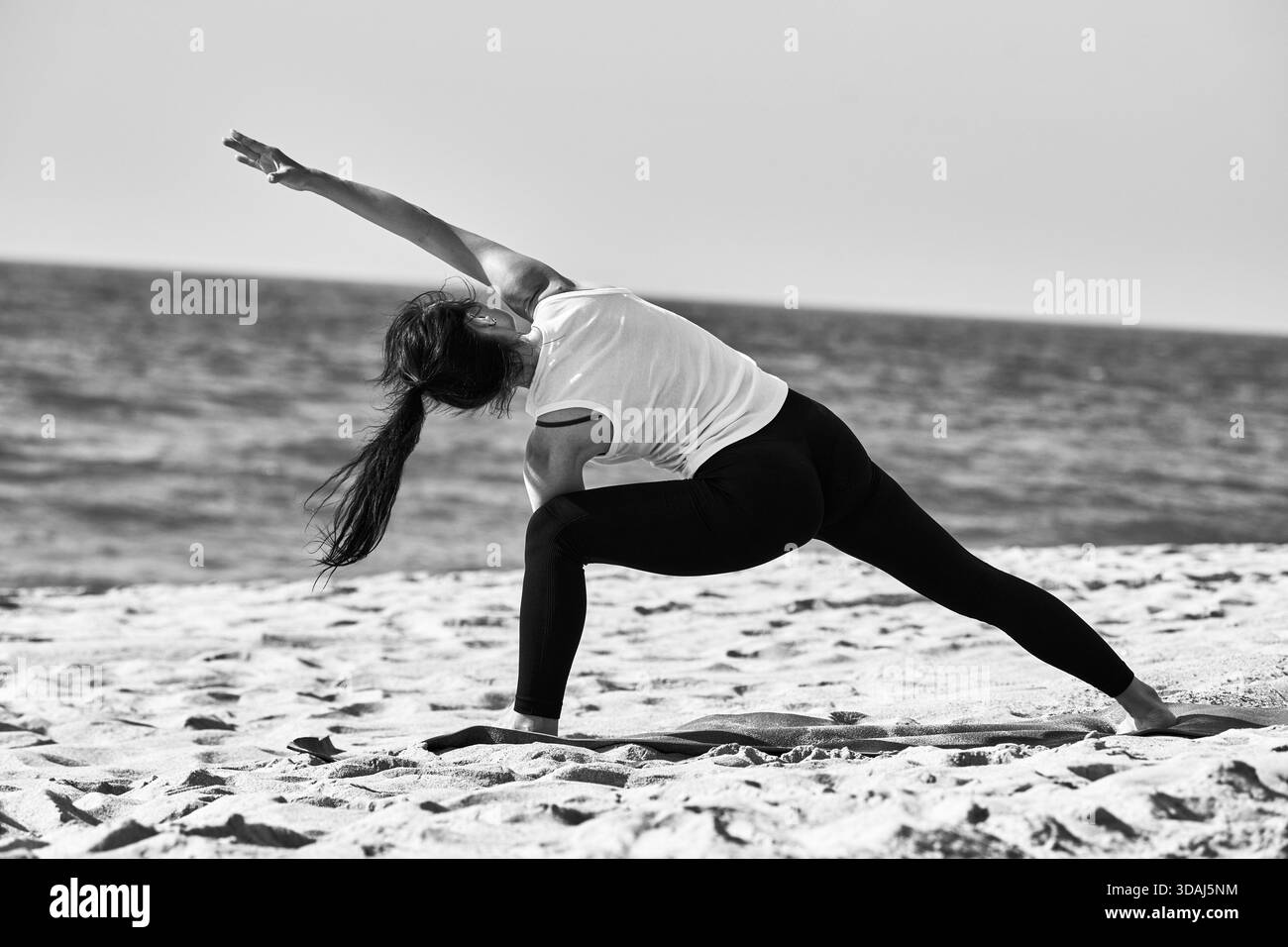 Jeune femme effectue le yoga stretch sur Sandy Beach près de la mer Baltique calme sous ciel clair. Concentrez-vous sur la pleine conscience et l'équilibre mis en valeur en extérieur Banque D'Images